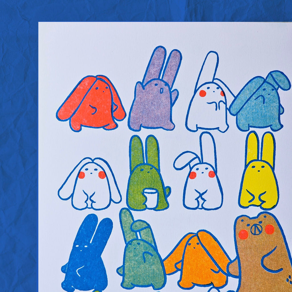 A white art print featuring a grid of colourful cartoon rabbits and creatures with blue outlines, displayed against a textured blue background.