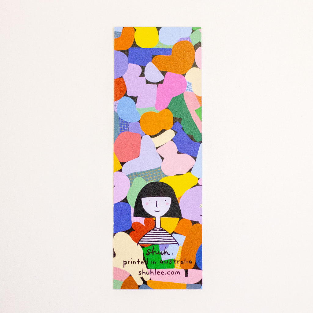 A trectangular bookmark featuring a colourful abstract pattern of overlapping shapes in pink, orange, yellow, green, blue, and purple, with a simple black-haired illustrated figure near the bottom. Handwritten text at the bottom reads 'shuh.', printed in australia and shuhlee.com