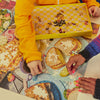 Two people working on a puzzle together, with one person wearing a yellow jacket and the other wearing a colourful sweater.