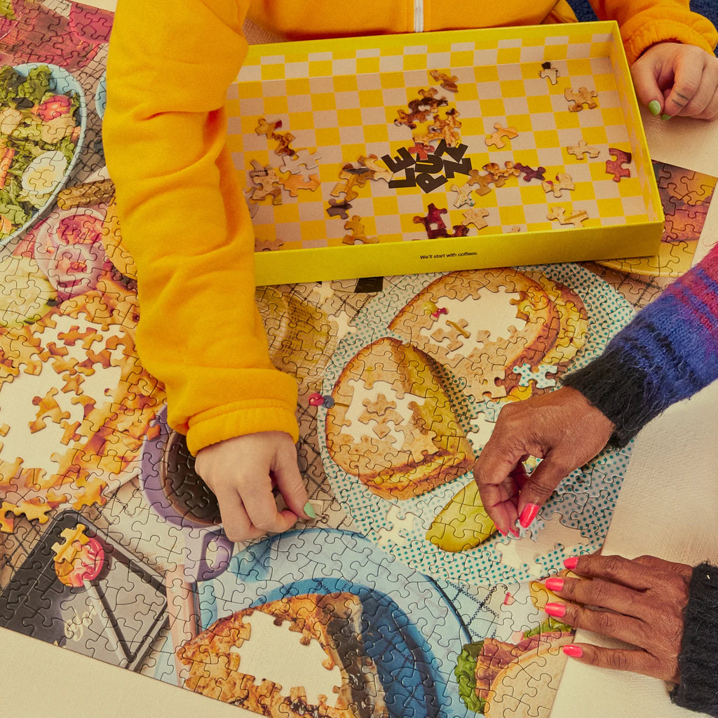 Two people working on a puzzle together, with one person wearing a yellow jacket and the other wearing a colourful sweater.