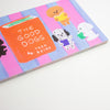 A rectangular notepad featuring a colourful illustration of several dogs reading books on pink and blue vertical stripes, with a central orange book reading 'THE GOOD DOGS' and 'by TADA REIKO'.