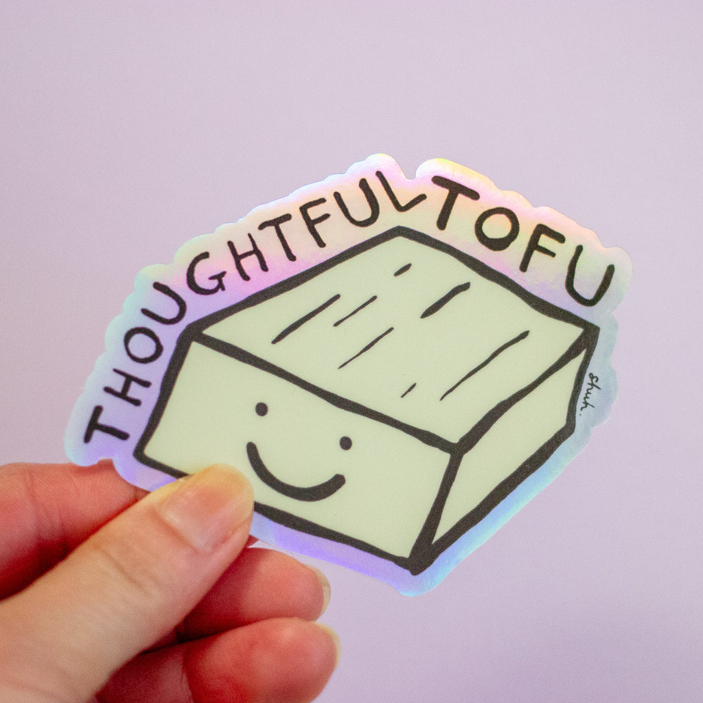 A hand holding a die-cut sticker featuring a smiling tofu block with the word 'THOUGHTFUL TOFU' in arched black lettering, against a soft lavender background.