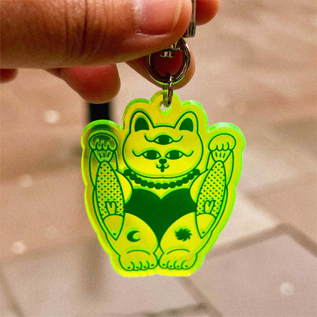 A hand holding a neon green cat with third-eye keychain.