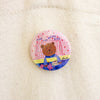 A round pin badge featuring a cartoon teddy bear sitting on a bed with the text 'TIME FOR BEDDY BYES' and a small 'shuh.' logo, pinned onto an off-white canvas tote bag.