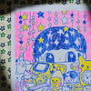 A colourful hand-drawn illustration on a white sheet of paper, featuring cartoon characters, stars, and a pink background, placed on a patterned surface.