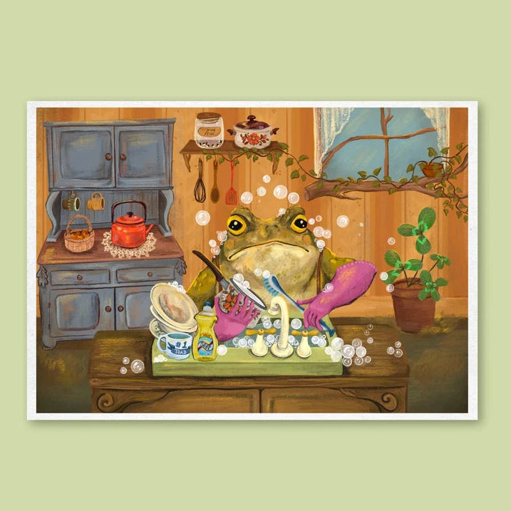 Art print featuring a whimsical illustration of a green frog washing dishes in a cozy kitchen setting, displayed against a solid light green background.