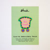Iron-on embroidery patch with a smiling face design on a green checkered card.