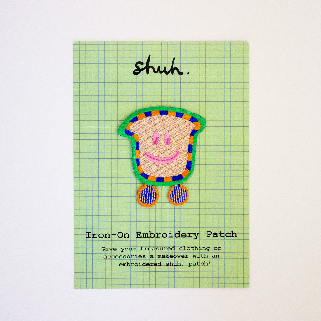 Iron-on embroidery patch with a smiling face design on a green checkered card.