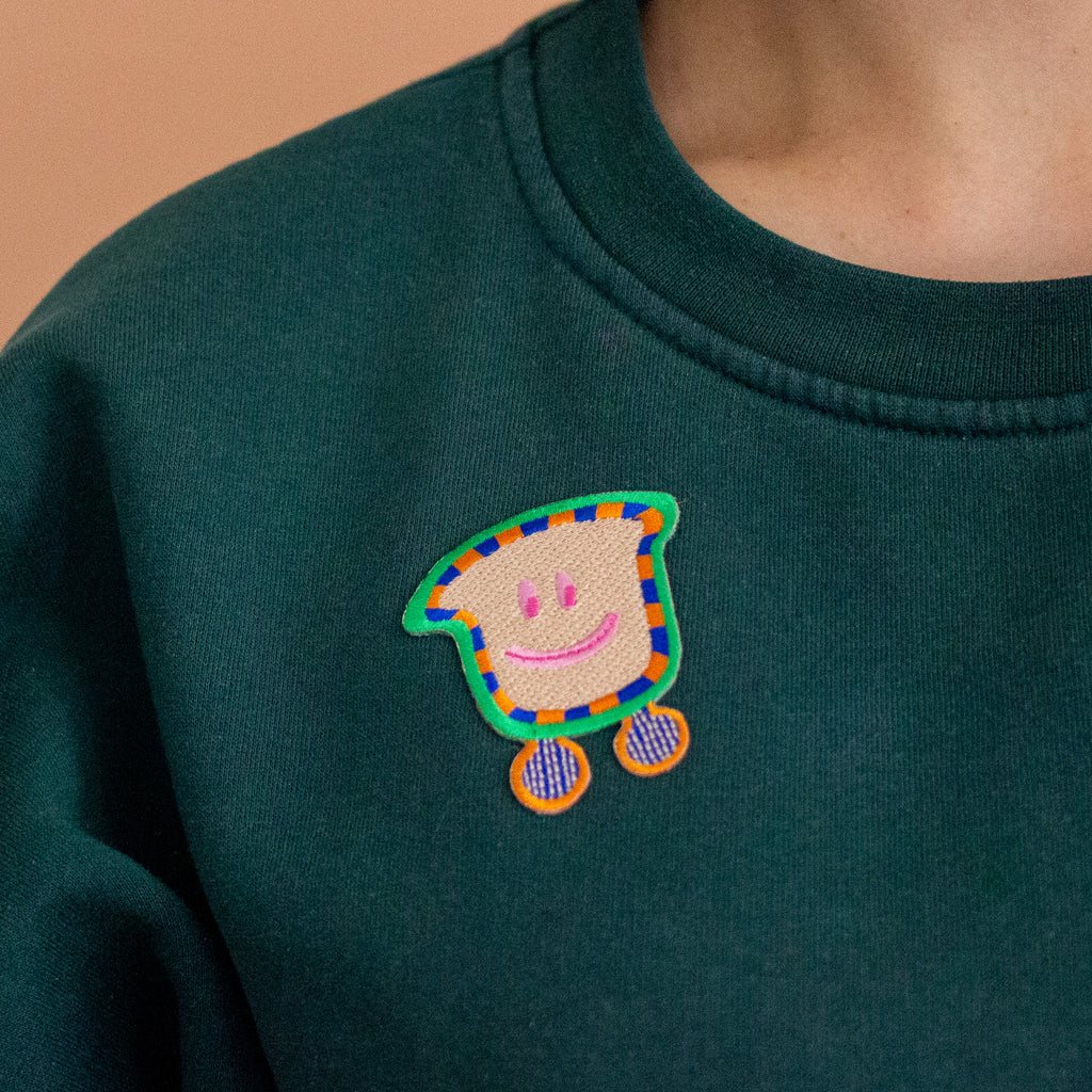 Green sweatshirt with a colorful embroidered patch on a peach background