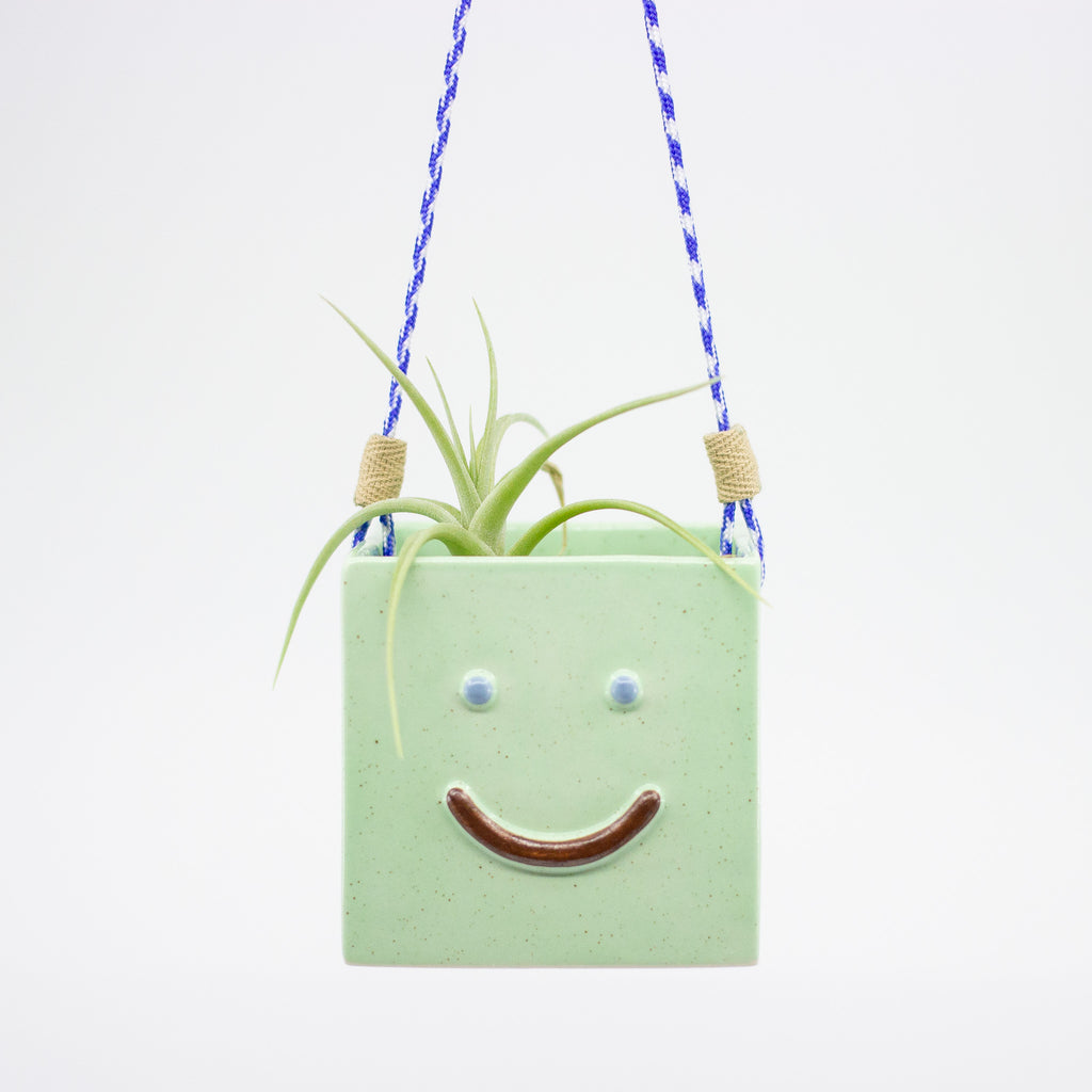 Green hanging planter with a smiley face design on a white background