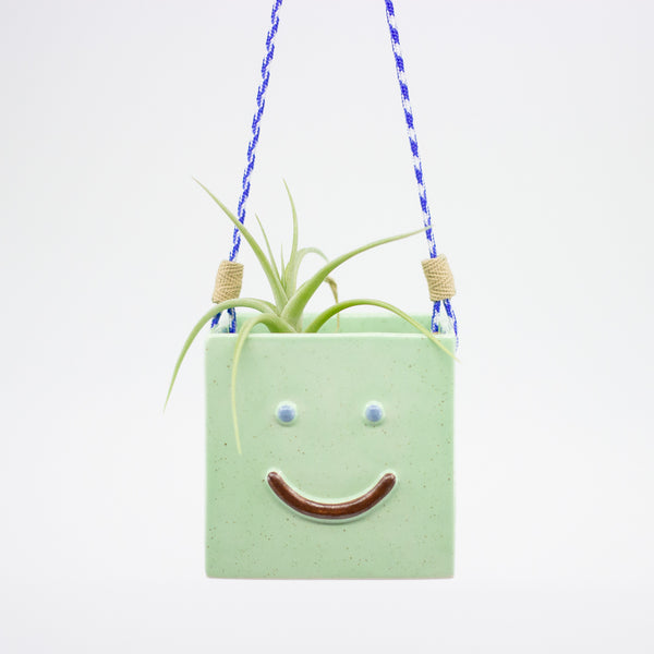 Green hanging planter with a smiley face design on a white background