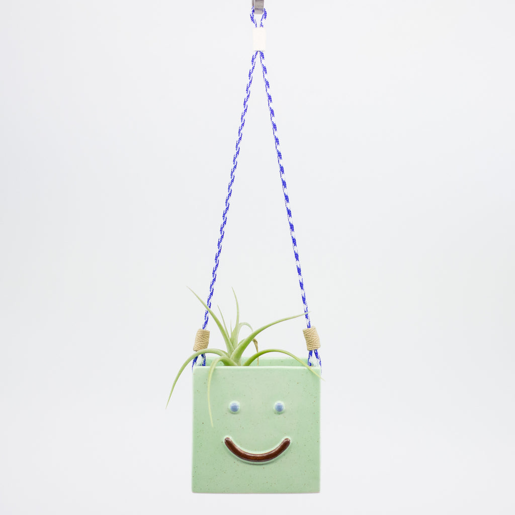 Green hanging planter with a smiley face design on a white background