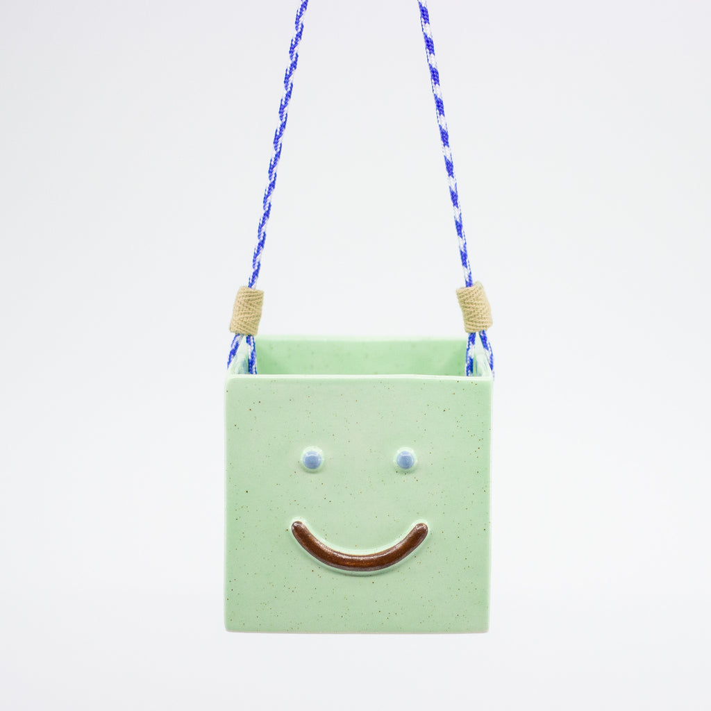 Green square-shaped hanging ornament with a smiley face on a white background