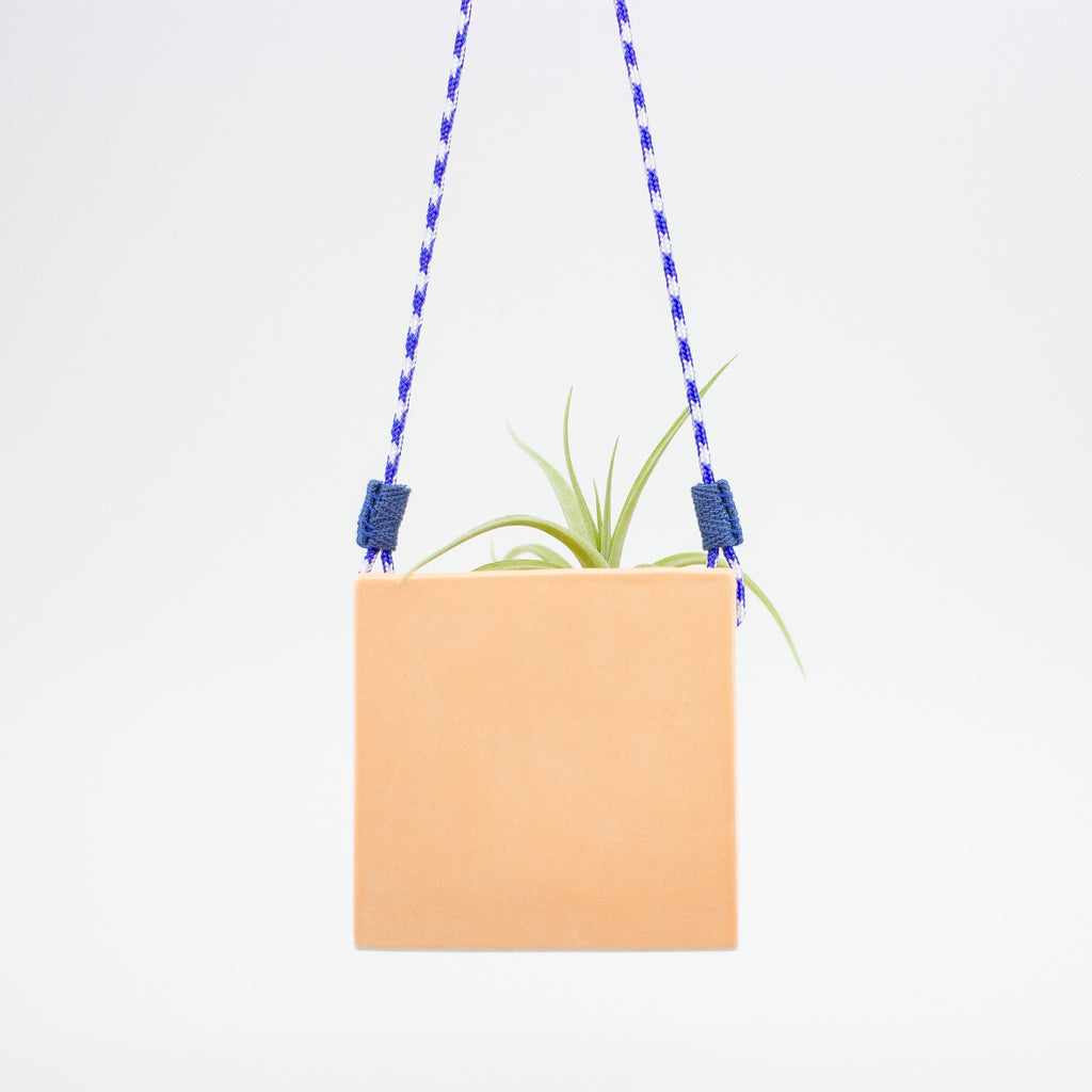 Square orange hanging planter with a blue and white rope on a light gray background