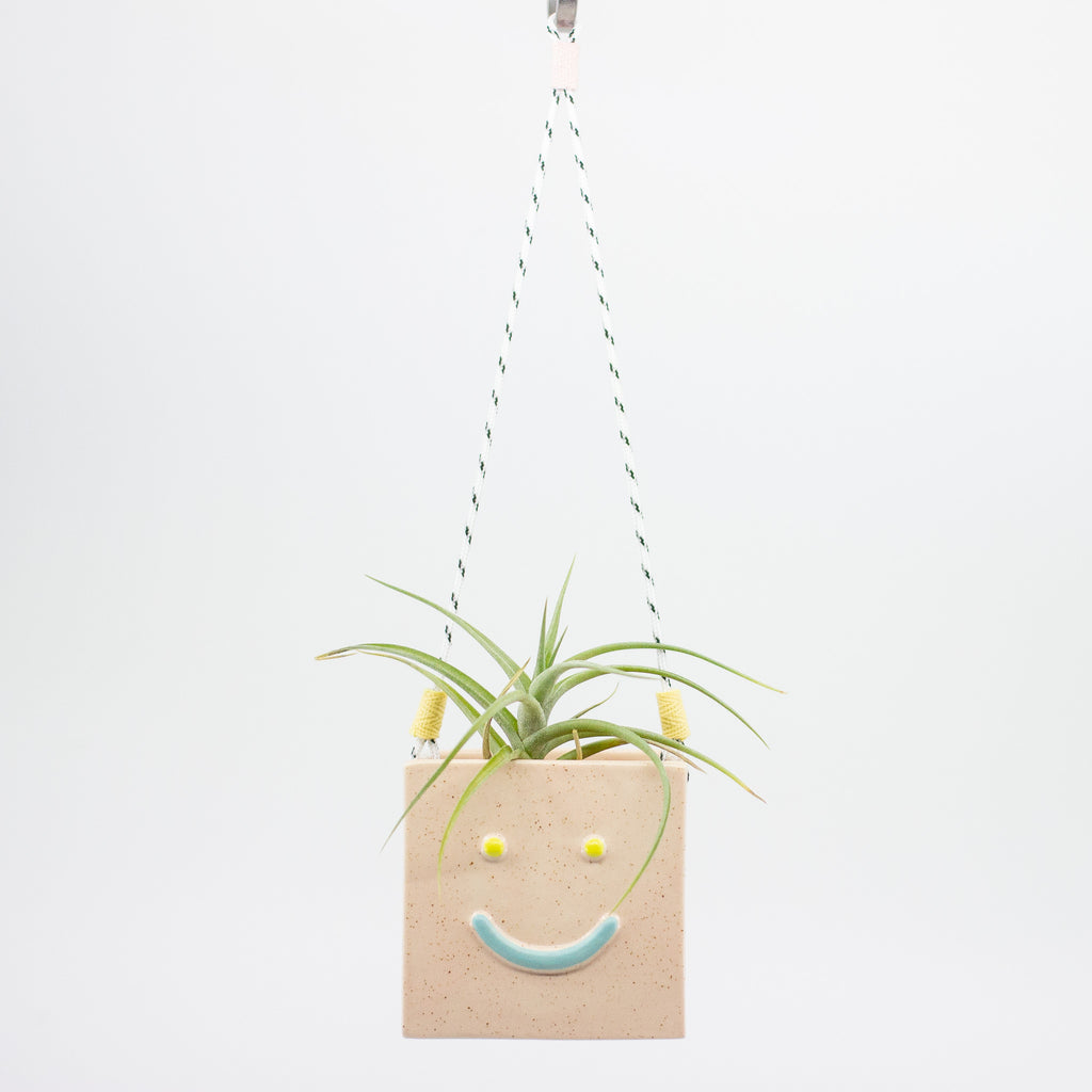 Square hanging planter with a smiley face design on a white background