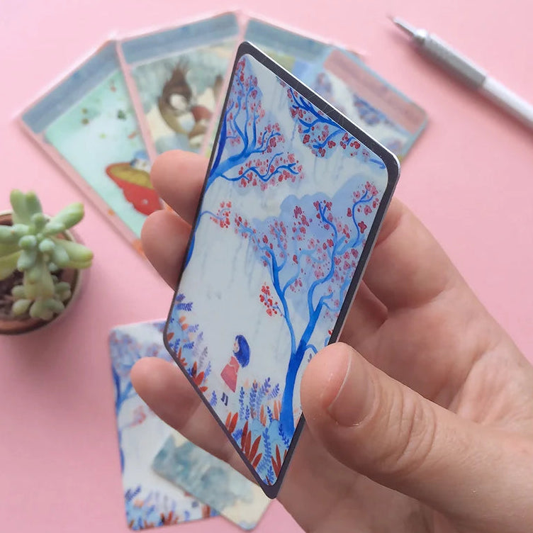 Hand holding a card with floral design on a pink surface with other cards and a ruler.