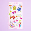 A sticker sheet  titled Trinkat Girlie featuring various colourful anime and pop culture keychain designs, displayed on a light purple background.