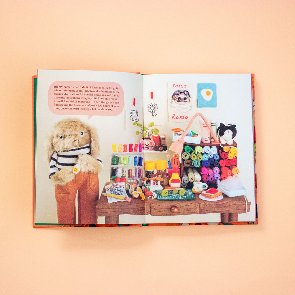 Open book with illustrations of a teddy bear, small figures, and colourful items on a table against a peach background.