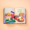 Open book showing a colourful figures of a fruit bowl and other fruits on a peach background