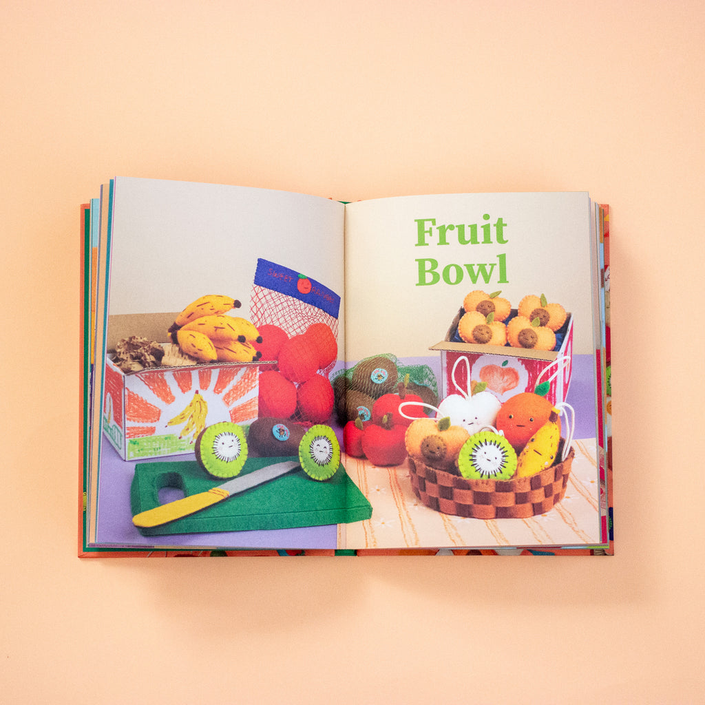 Open book showing a colourful figures of a fruit bowl and other fruits on a peach background