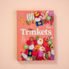 Book titled 'Trinkets' with colourful felt toys on a peach background