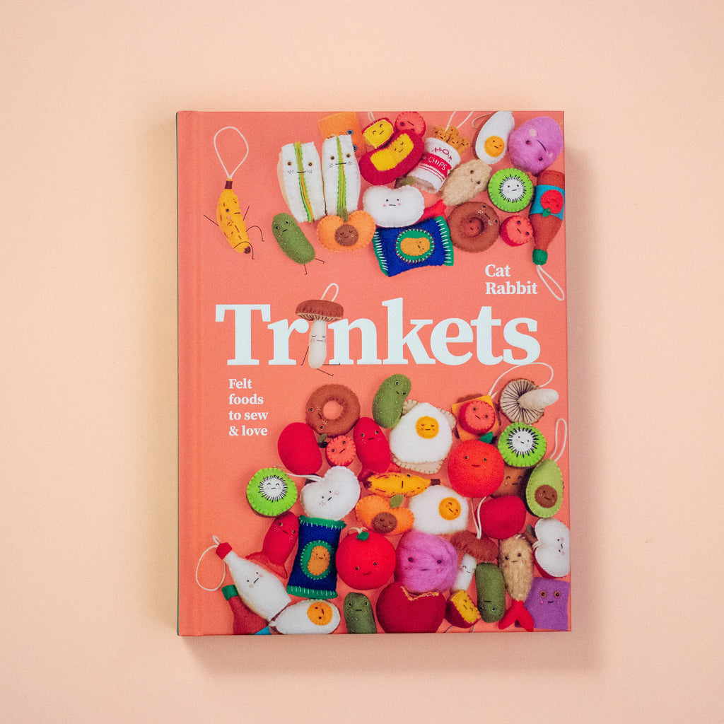 Book titled 'Trinkets' with colourful felt toys on a peach background