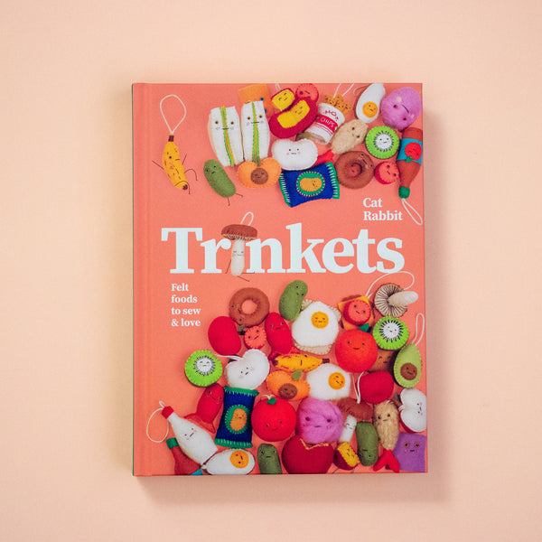 Book titled 'Trinkets' with colourful felt toys on a peach background