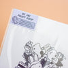 A close-up of a printed sheet corner with a visible label reading 'BY IMI PRINT SHOP' and cartoon characters printed in black on a white surface, set against a peach background.
