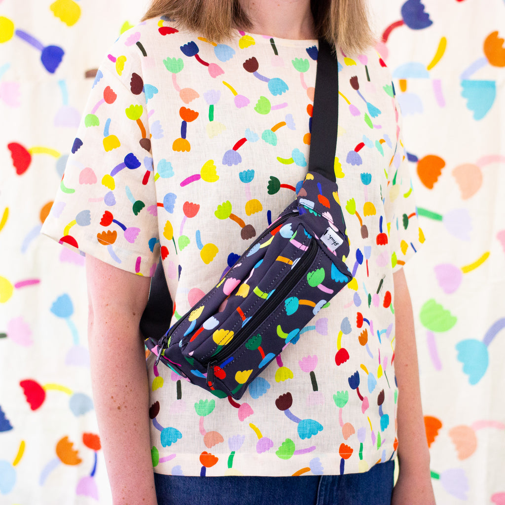 Model carrying the tulip bumbag over their shoulder. The Tulip print is a playful and colourful series of multicoloured tulip motifs on a black background.&nbsp;
