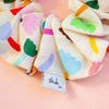 Colourful floral scrunchie on a peach background, featuring a 'shuh' label.