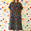 A front view of the Tulip linen dress. Multicoloured tulips on a black background. Models hands are in the pockets. 