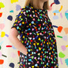 A neck view of the Tulip linen dress. Multicoloured tulips on a black background. Models hands are in the pockets. 