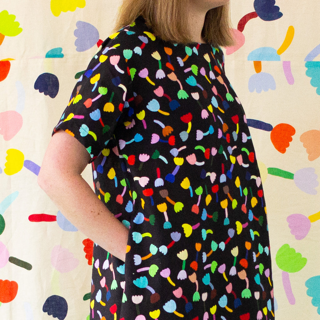 A neck view of the Tulip linen dress. Multicoloured tulips on a black background. Models hands are in the pockets. 