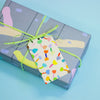 A closeup of the shuh. tulip gift tag attached to a green string on a gift box. Print features multicoloured tulips.