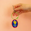 Hand holding a keychain with a colourful design on a peach background