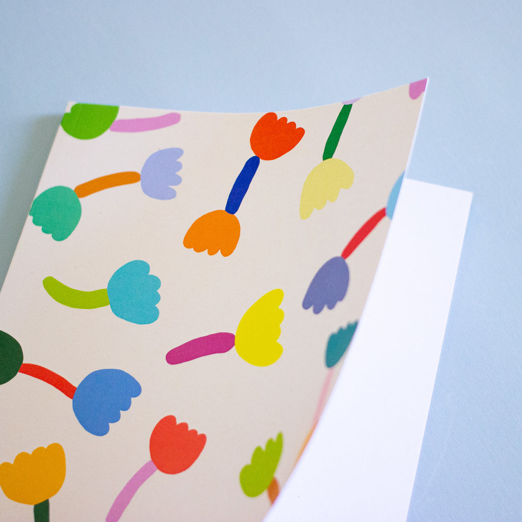 Front view of the tulip notebook. Cover has multicoloured tulip motif on cream background. Also shows inside with blank white pages. 