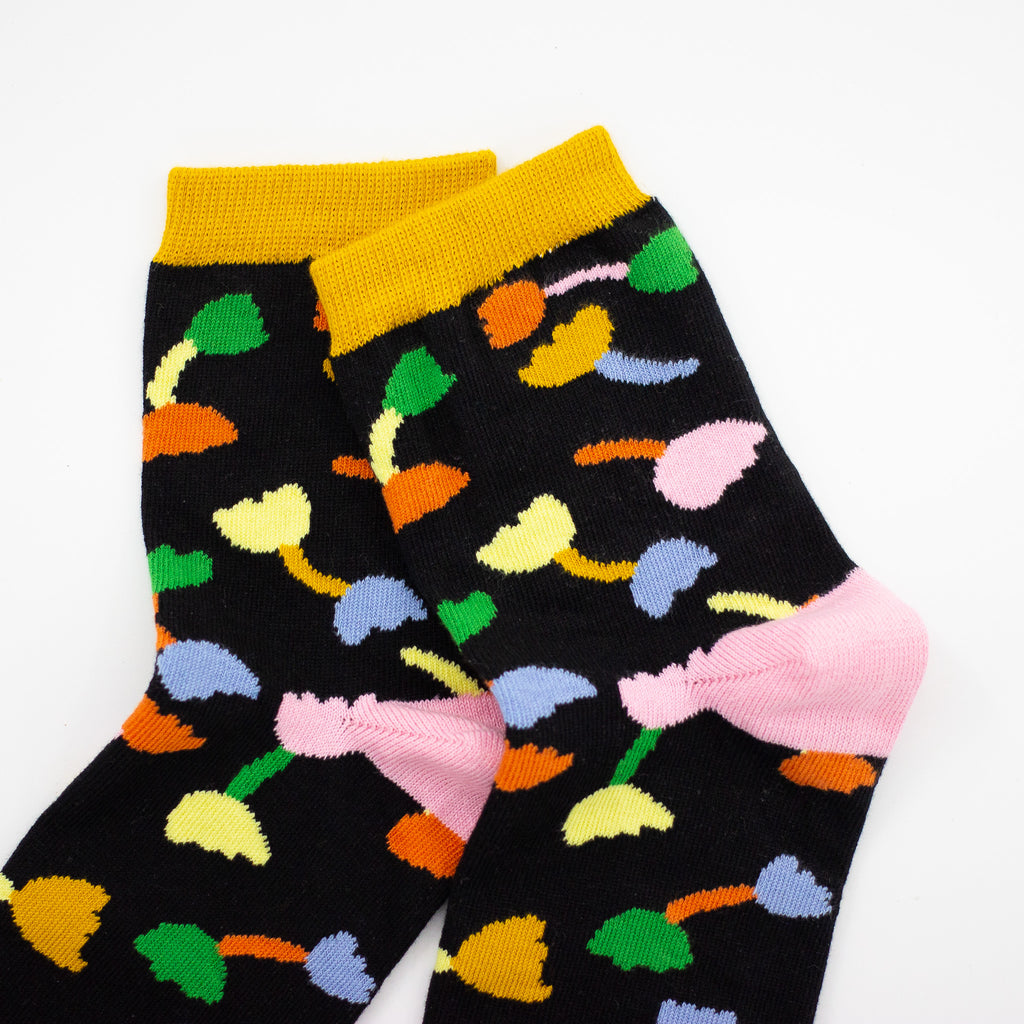 A closeup side view of the shuh. Tulip socks. Pink heel, green toe, black background and muliticoloured tulip motifs. 