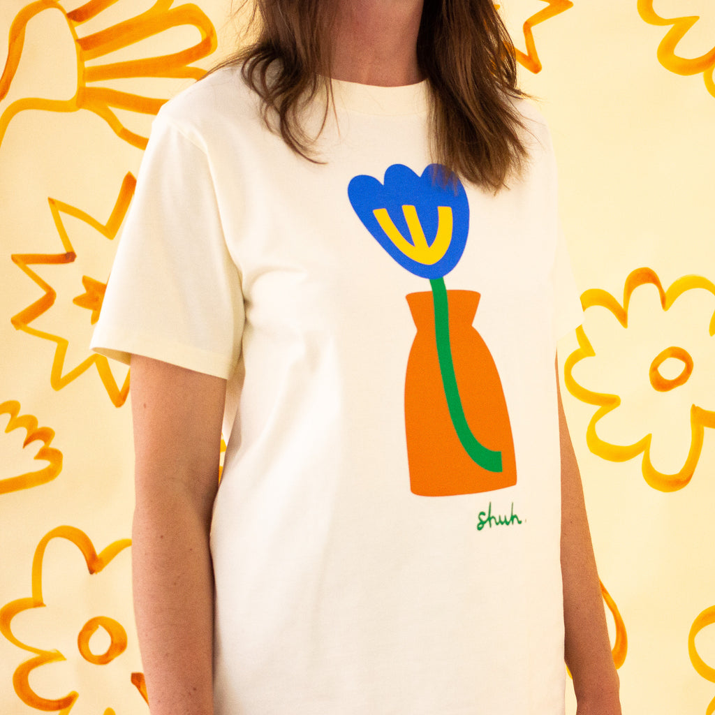 Side view of the Tulip Tee - blue flower, green stem, in an orange vase. Stylised and imaginative. 