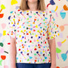 A Front view of a model wearing the tulip linen top in cream background. Repeating tulip motifs in multicoloured patterns. 