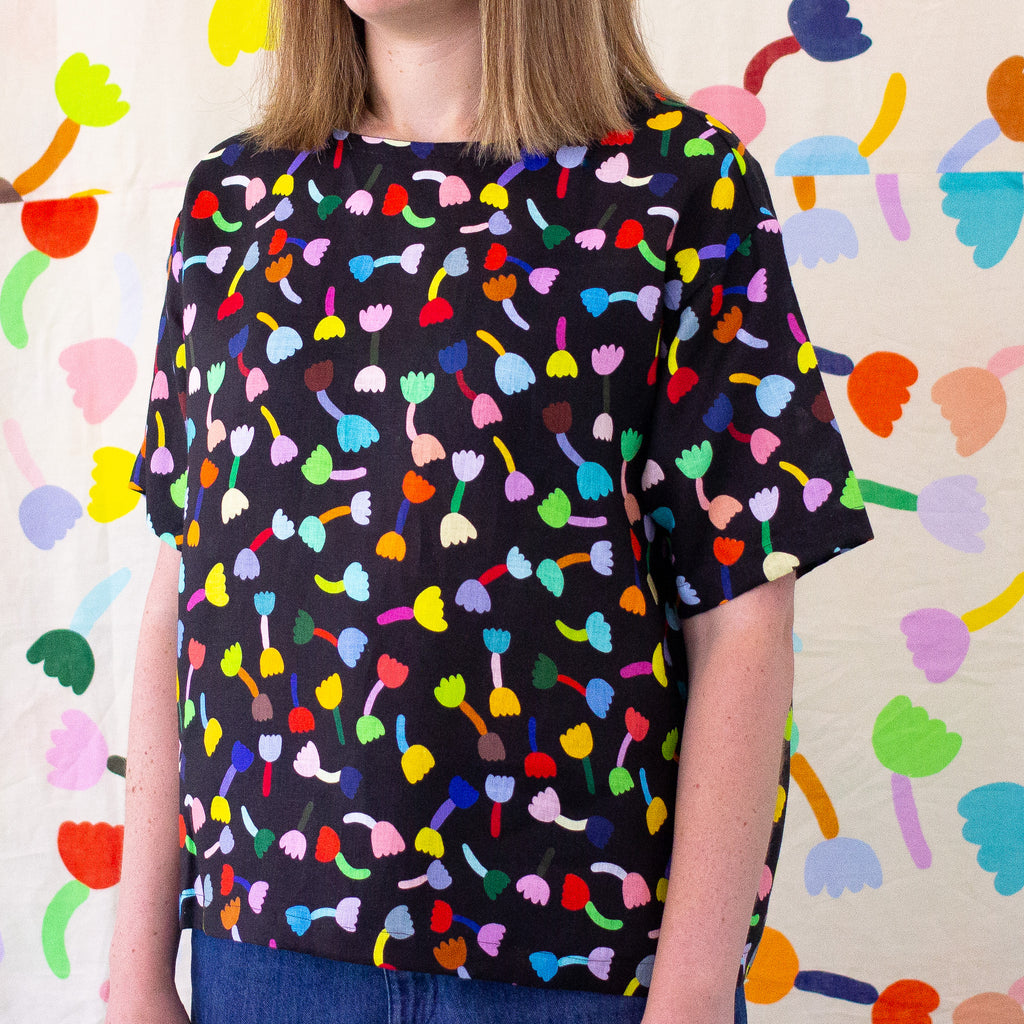 A Front view of the Tulip Linen top, with black background. Multicoloured repeated tulip motifs. 