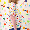 A side view of a model wearing the tulip linen top in cream background. Repeating tulip motifs in multicoloured patterns. 