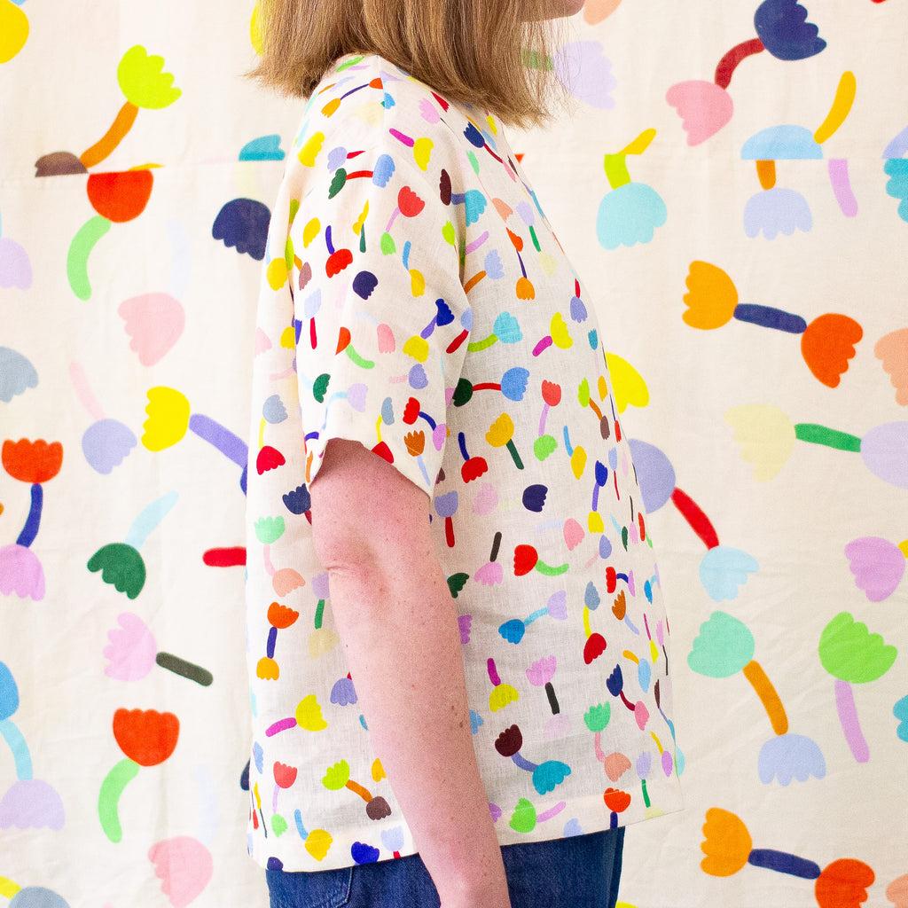 A side view of a model wearing the tulip linen top in cream background. Repeating tulip motifs in multicoloured patterns. 