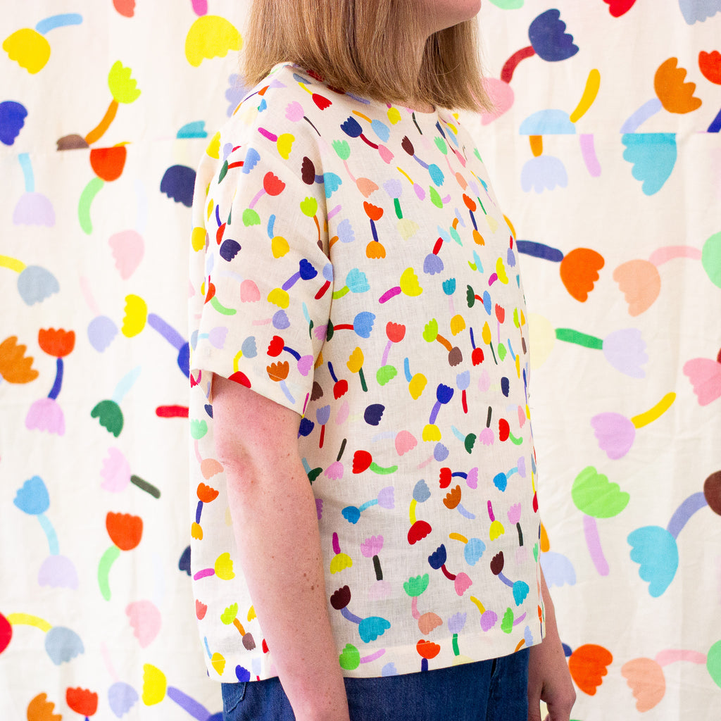 A Side view of a model wearing the tulip linen top in cream background. Repeating tulip motifs in multicoloured patterns. 