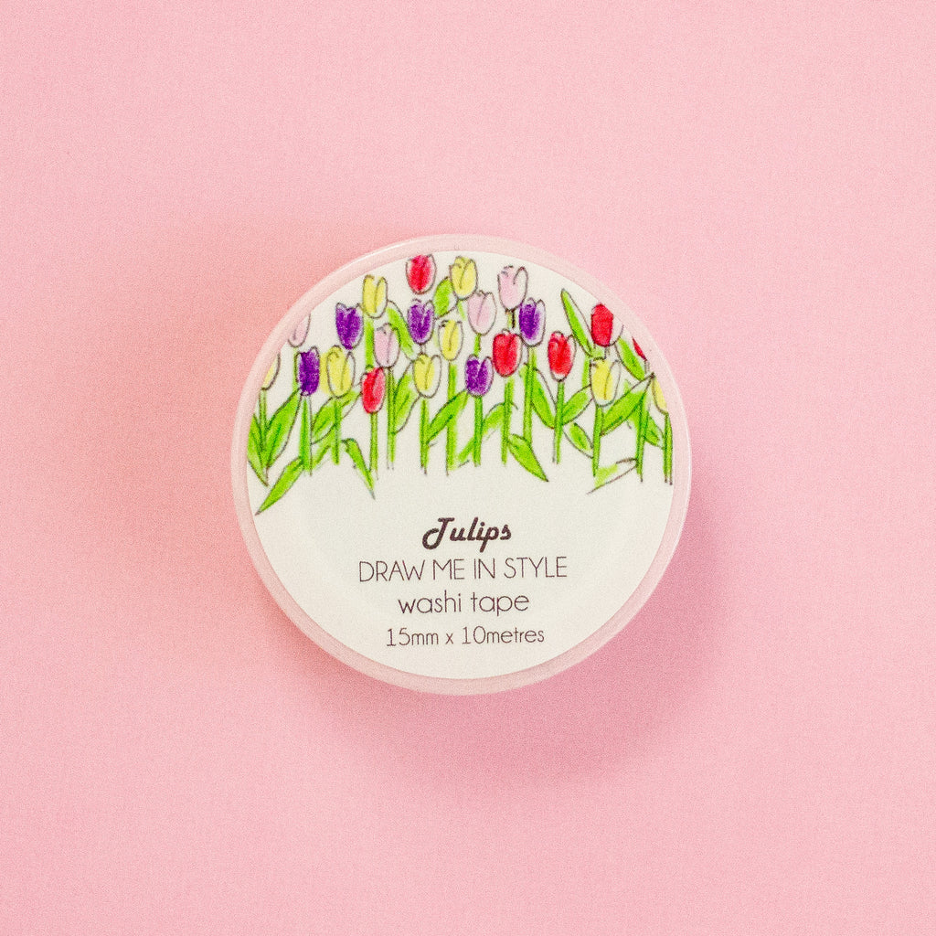 A round container of Tulips Washi Tape by Draw Me In Style, featuring a colourful tulip illustration on a white background, set against a solid pink backdrop.