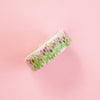 A roll of washi tape featuring a colourful tulip field pattern on a white background, set against a solid pink backdrop.