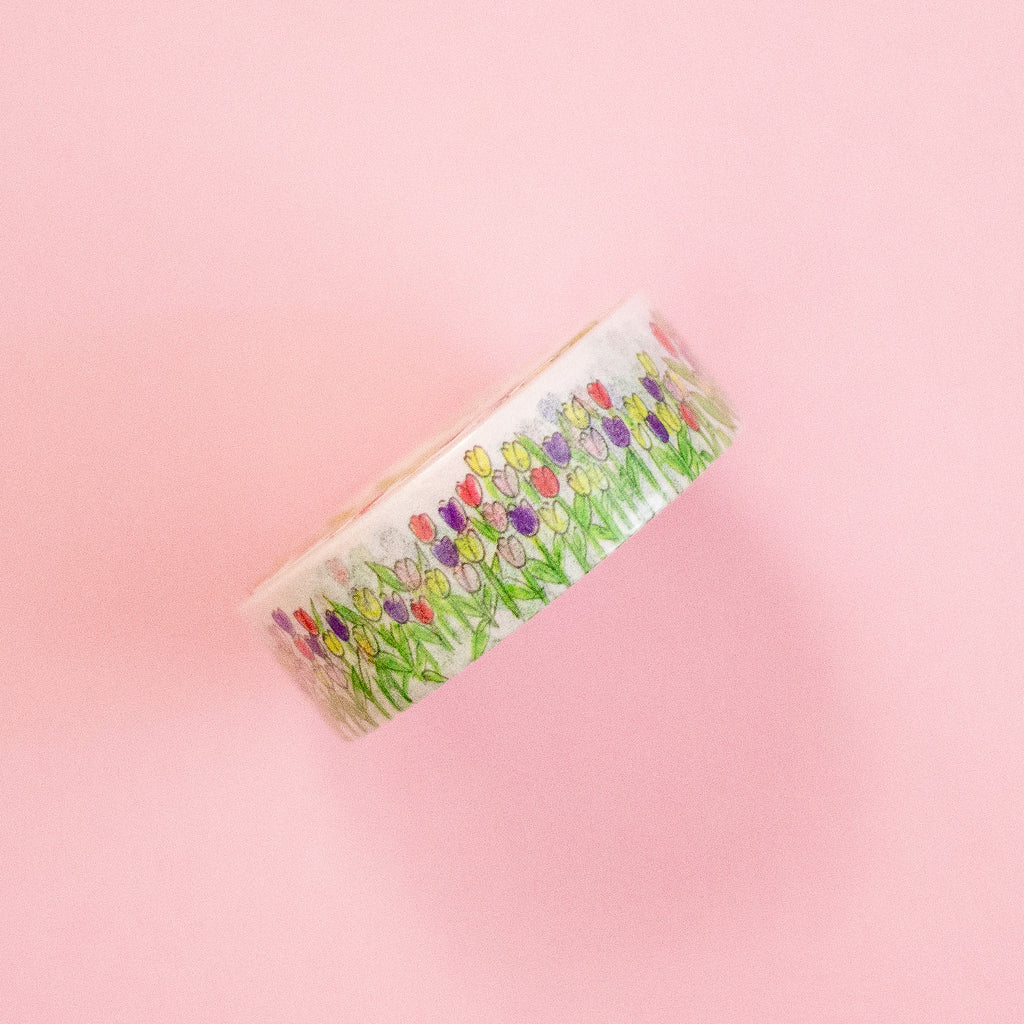 A roll of washi tape featuring a colourful tulip field pattern on a white background, set against a solid pink backdrop.