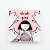 Enamel pin showing two hand-drawn cats sitting on the shoulders of a girl in a striped tee, displayed on a pink backing card with illustrated cats and “shuh. pins” branding.