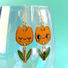 Orange tulip-shaped earrings with face and green leaves on a clear glass with teal background