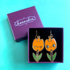 Orange tulip-shaped earrings with green leaves in a purple box on a teal background