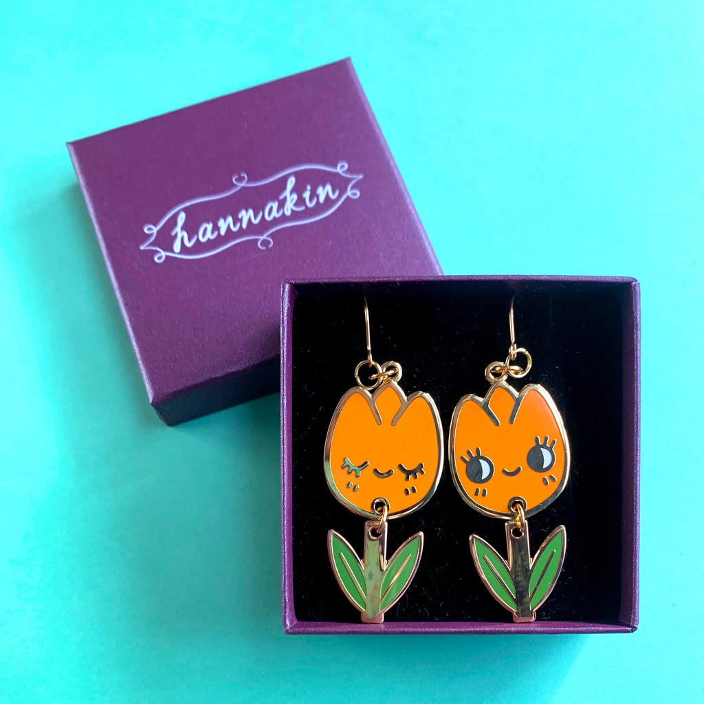 Orange tulip-shaped earrings with green leaves in a purple box on a teal background